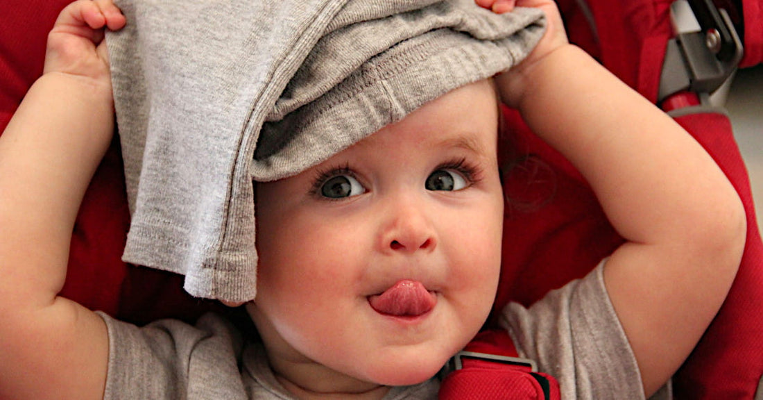 Photo d'un bébé garçon souriant jouant avec un vêtement en coton bio, illustrant le choix de la bonne taille pour des vêtements bébé haut de gamme