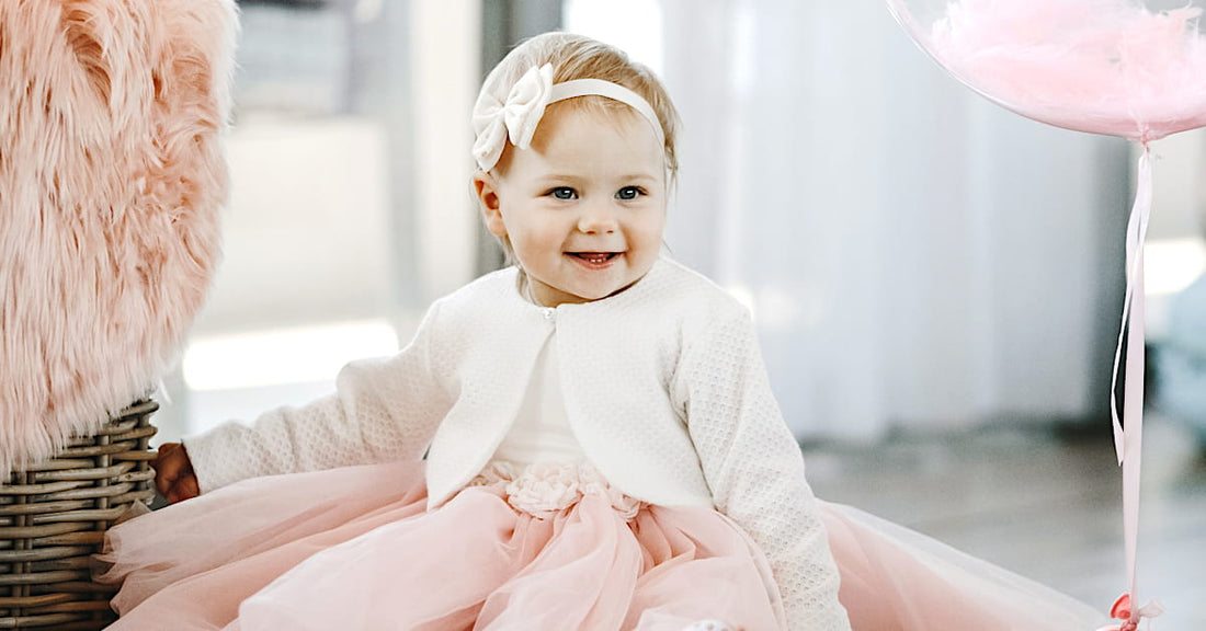 Bébé fille habillé en tenue chic avec un bandeau à gros nœud, assis dans un décor lumineux