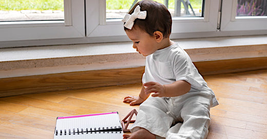 Bébé fille avec un cahier pour s'imaginer qu'elle prend connaissance des prénoms filles les plus tendances pour 2025