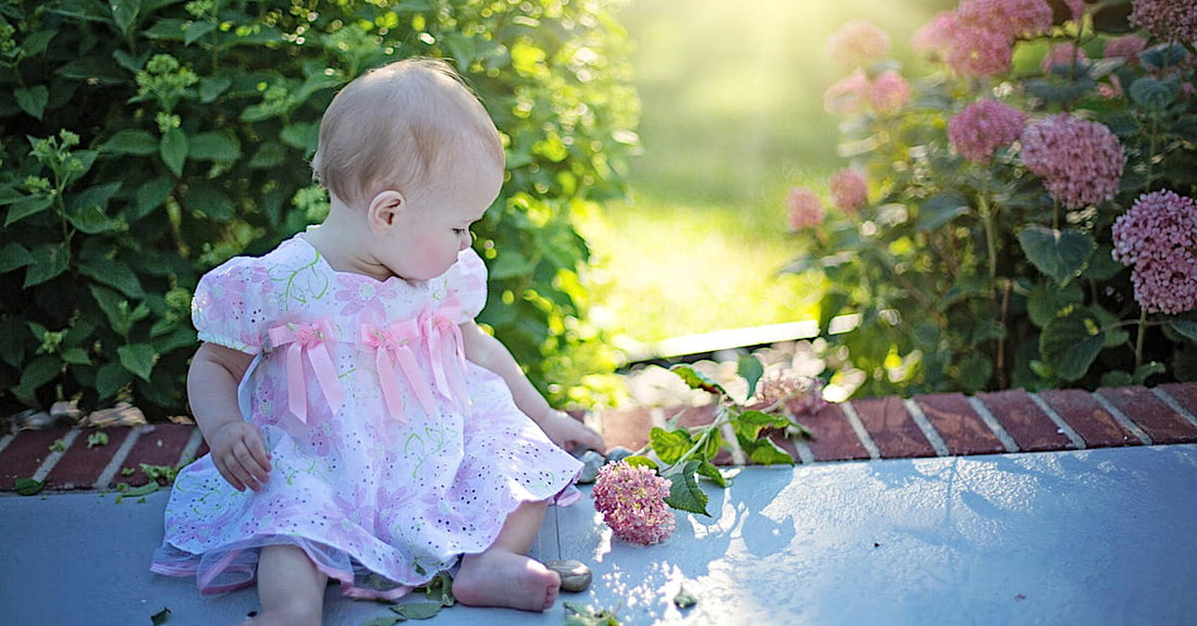 Photo d'un bébé fille habillé d'une robe élégante, blanche imprimé fleuri et détail noeuds, parfaite pour une occasion comme un mariage ou un baptême