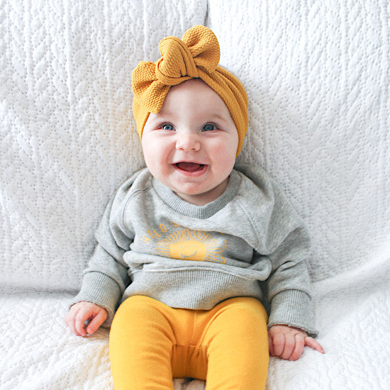 Bébé fille souriante en ensemble gris et jaune, sweatshirt motif soleil et legging moutarde