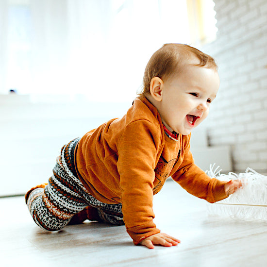 Bébé garçon en ensemble tricot marron et noir, rampant au sol dans une pièce lumineuse