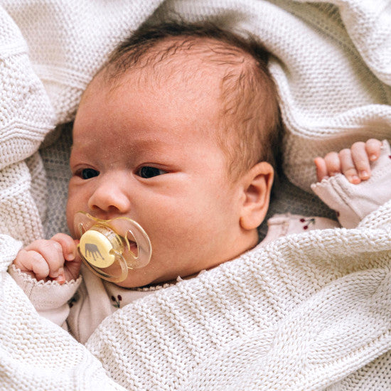 Nourrisson allongé sous une couverture tricotée beige, tétine en bouche