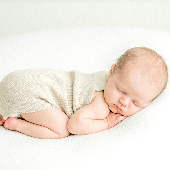 Nouveau-né endormi dans une tenue naissance beige en maille, ambiance douce et épurée
